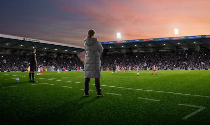 A woman standing on a soccer field in a parka.