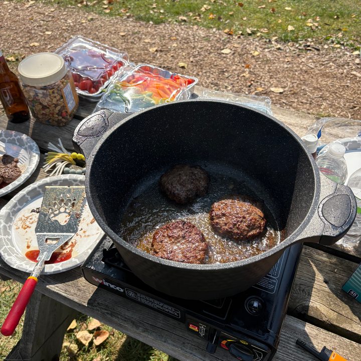 A photo of burgers being cooked outside at a campsite, taken with the iPhone 16.