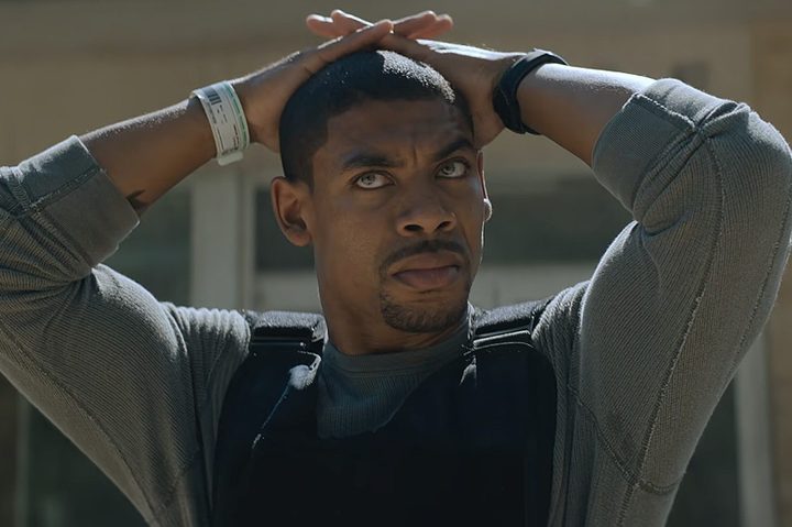 A man kneels down with his hands on his head.