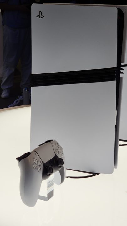 A side view of a vertical PS5 Pro, with a matching controller propped up next to it