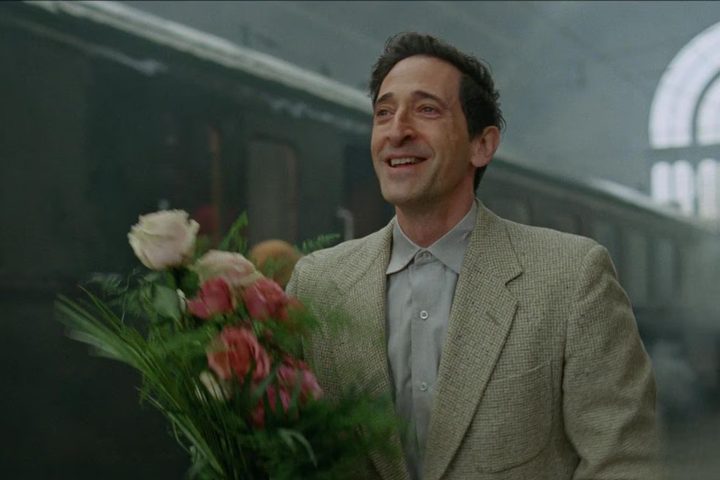 Adrien Brody carries a bouquet of flowers in The Brutalist.