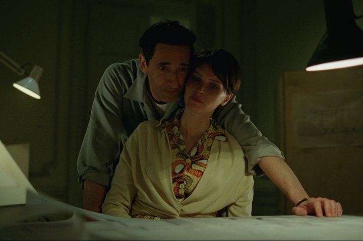 Adrien Brody stands behind Felicity Jones in The Brutalist.
