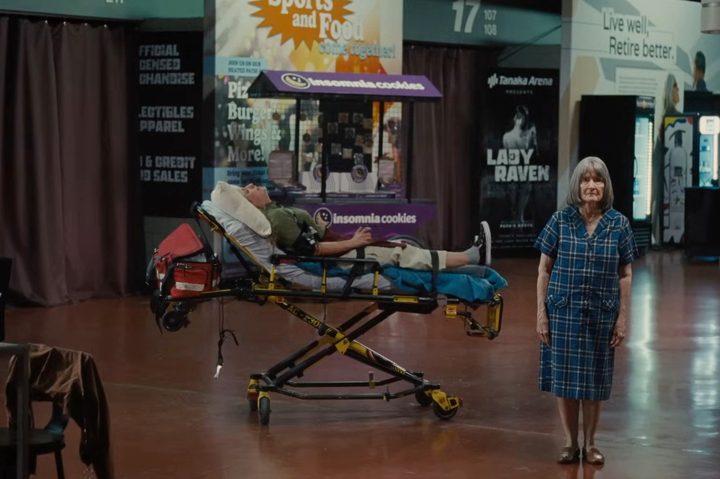 An elderly woman stands near a girl on a stretcher in Trap.