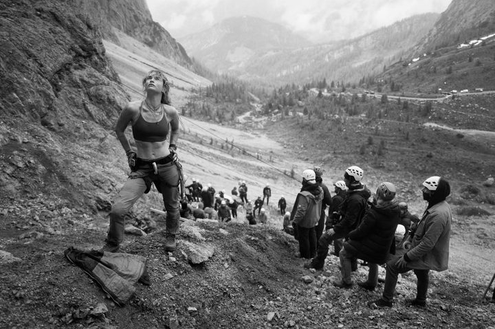 Lily James stands at the base of a cliff with people standing near her.