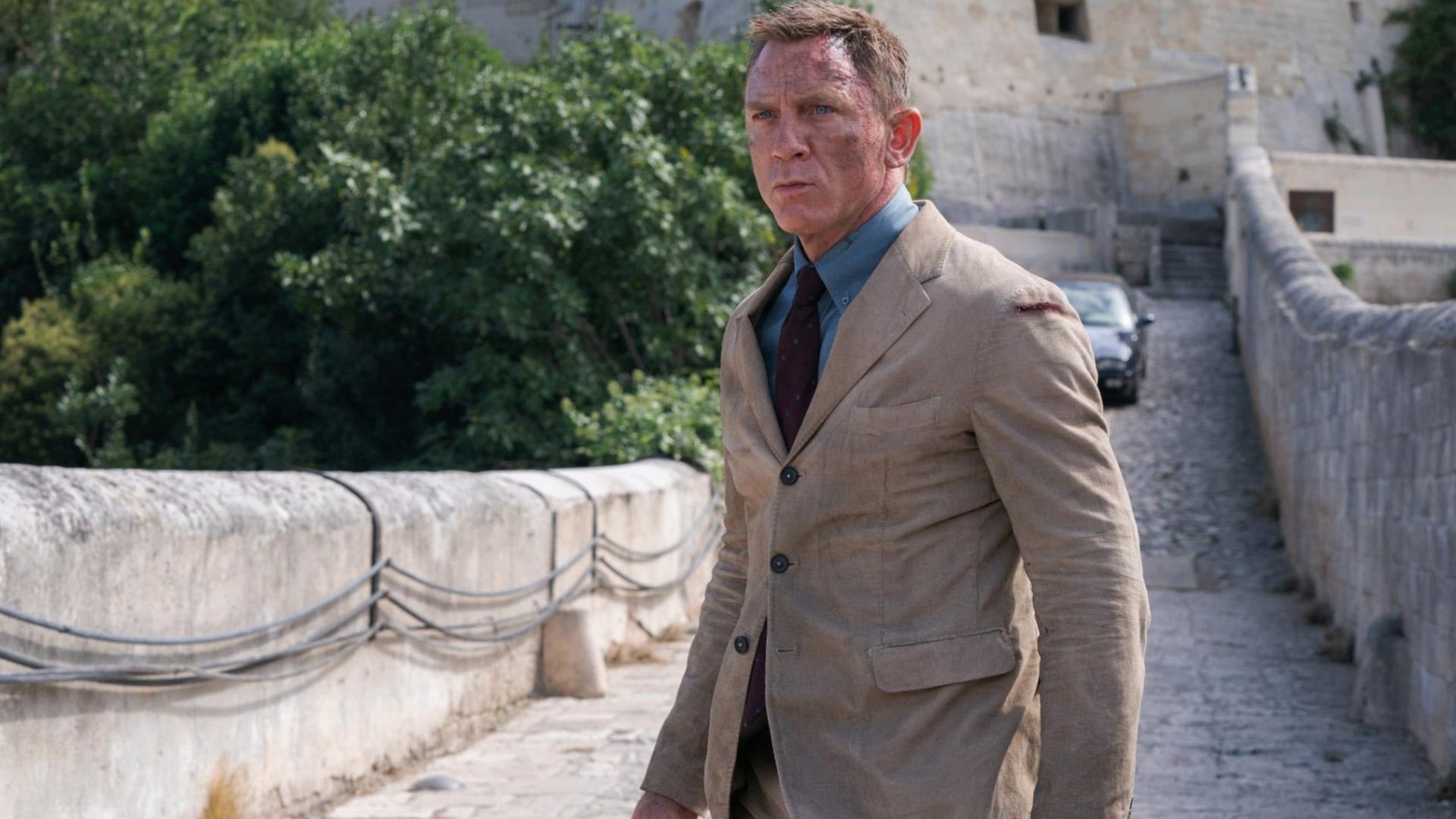 A dirtied James Bond stands on a road.
