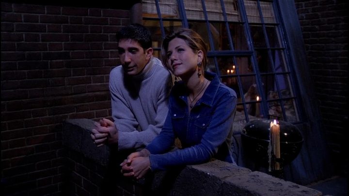 David Schwimmer and Jennifer Aniston as Ross and Rachel standing outside a balcony and looking up in Friends.