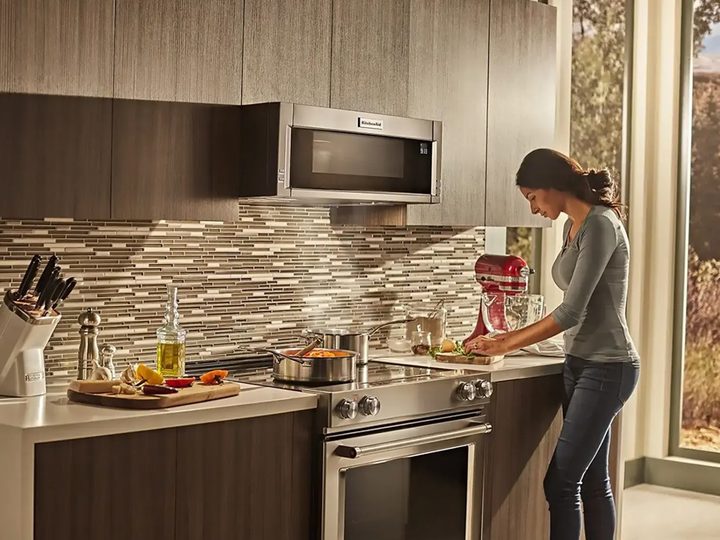 A woman stands at a counter near an installed KitchenAid 6.4 cu. ft. electric convection range.