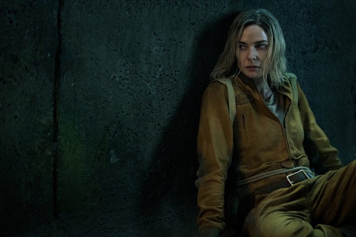 A woman leans against a wall in Silo.