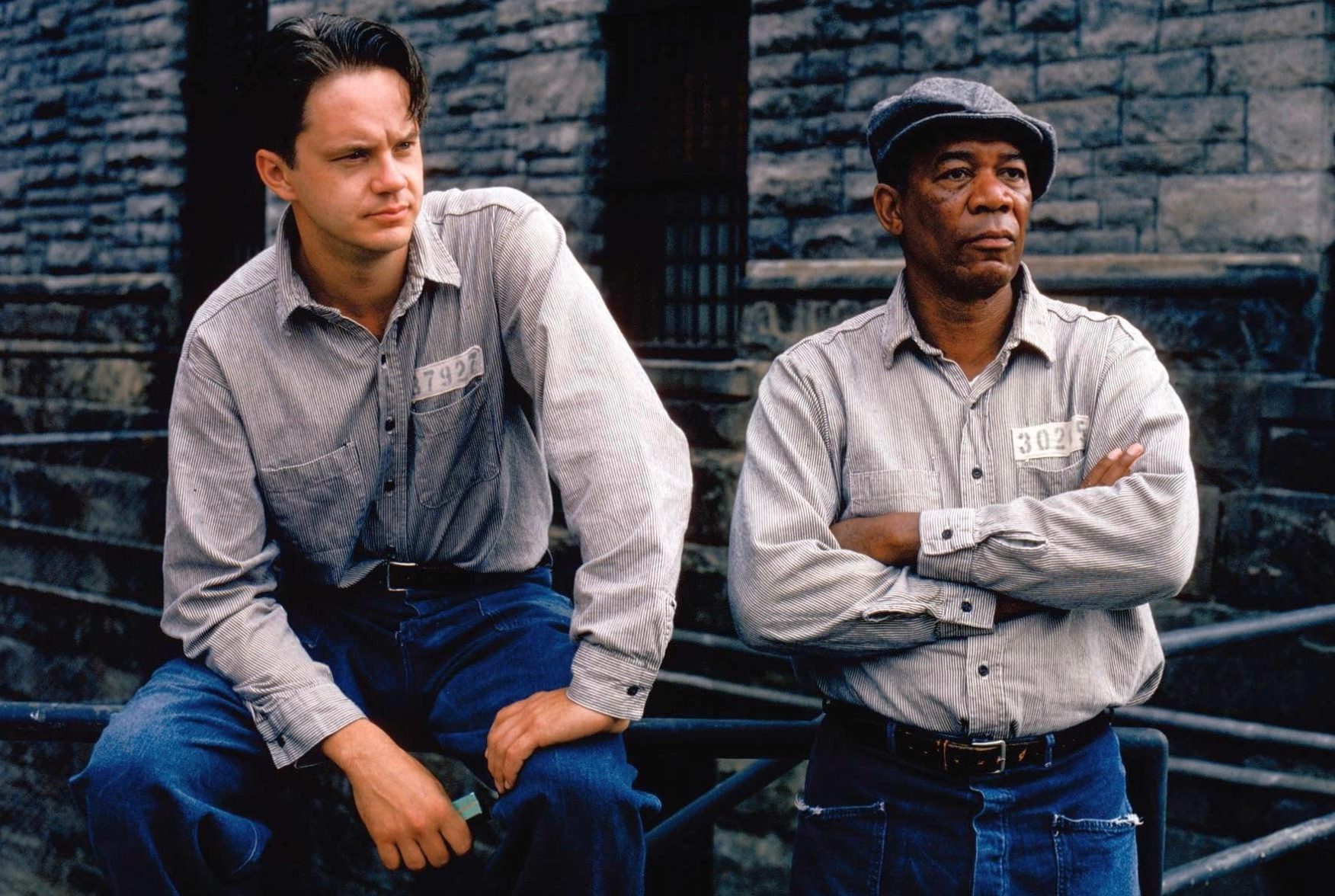 Two prisoners sit down next to each other on a bench.