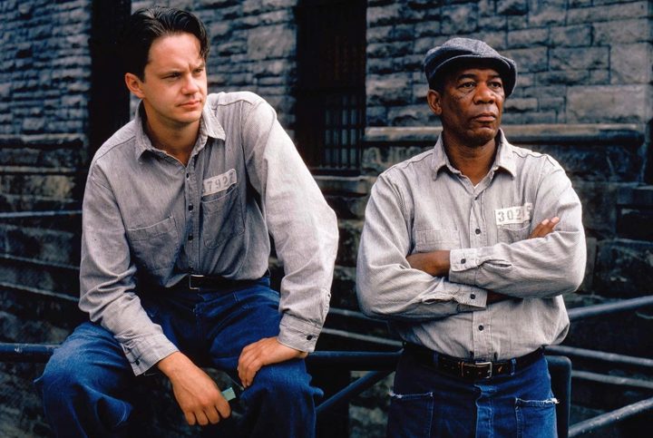 Two prisoners sit down next to each other on a bench.