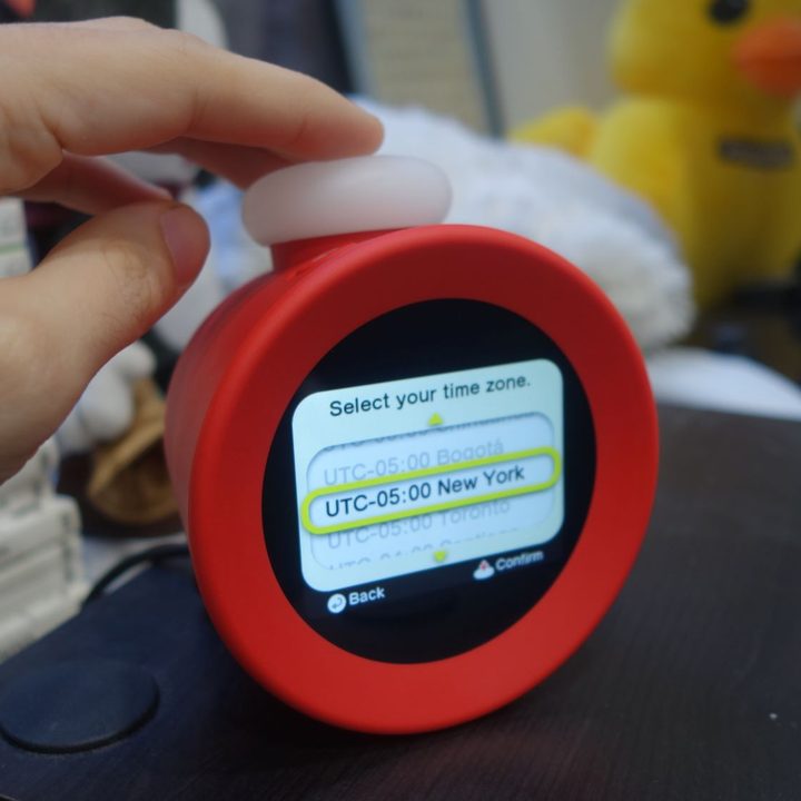 A hand presses the top button of the Alarmo.