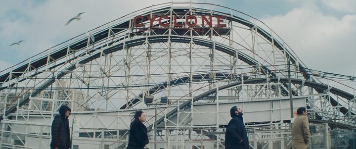 Four people walk near a rollercoaster in Anora.