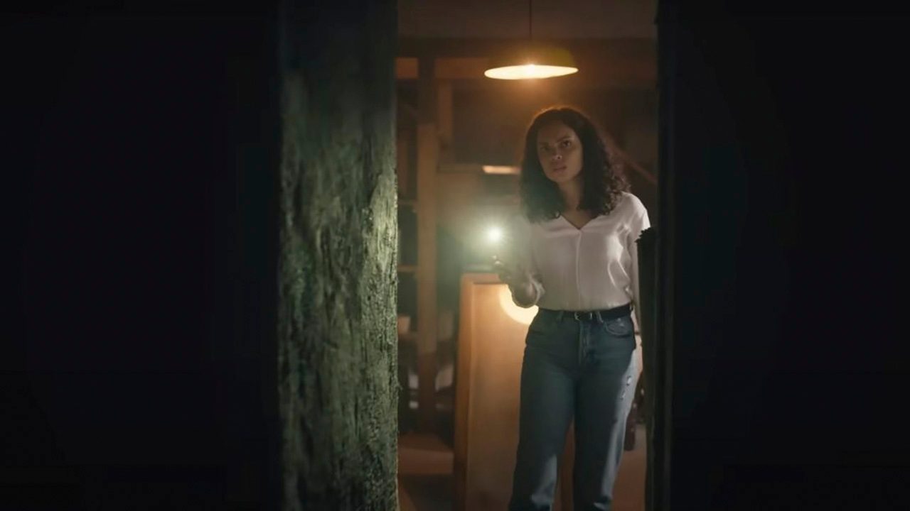 A woman looking through a dark doorway with a flashlight in Barbarian.