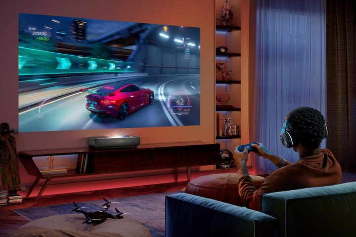 The Hisense PL2 ultra short throw projector with a gamer playing a game.