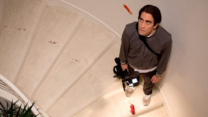 A man holds a camera in a white staircase in Nightcrawler.