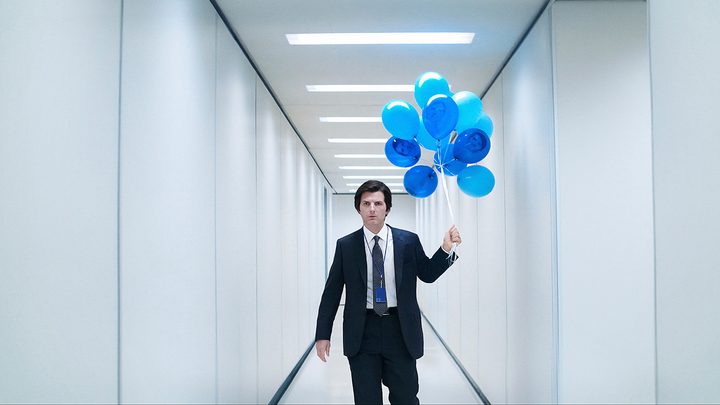 Mark walking down the bright white hallway at work looking angry, carrying a bunch of bright blue balloons in Severance.