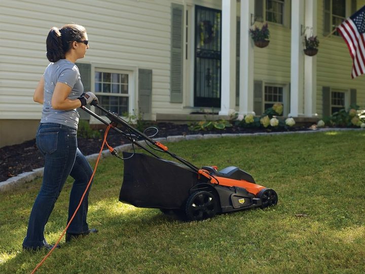 A woman pushes the Black+Decker corded lawn mower across her yard.