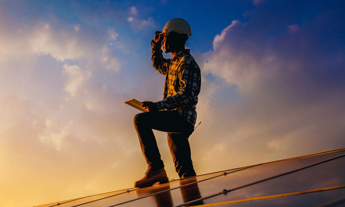 Promotional image for Tech For Change. Person standing on solar panel looking at sunset.