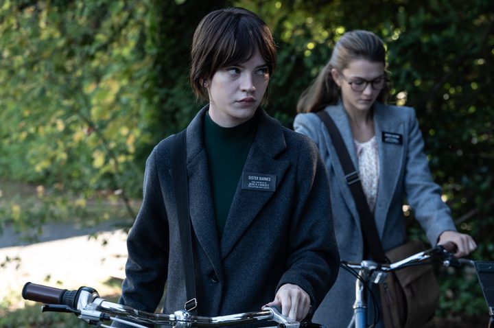 Two girls hold their bikes and walk.