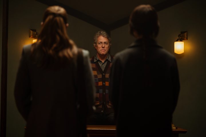 Hugh Grant stands in front of two women in Heretic.
