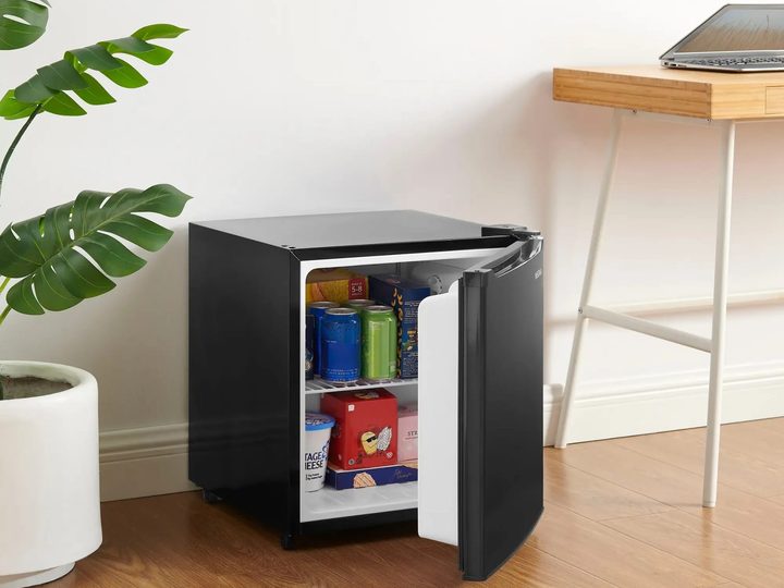 A 1.7 cu. ft. Insignia Mini Fridge nestled between a houseplant and a laptop desk.