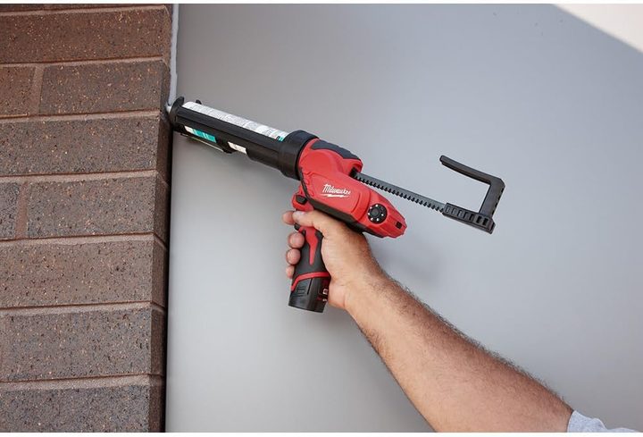A man uses a Milwaukee M12 Caulk Gun to seal up a joint between drywall and brick.