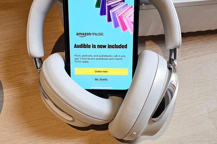 An iPhone with Bose headphones showing the Amazon Music app with a promotional message for Audible audiobooks.
