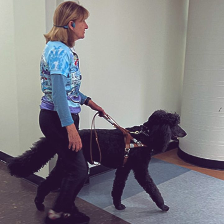 A blind woman walking with a dog in a building.