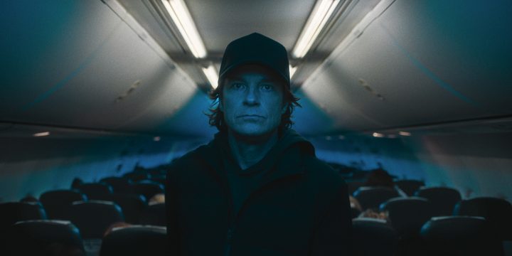 A man in a black hat walks up the airplane's aisle in Carry-On.