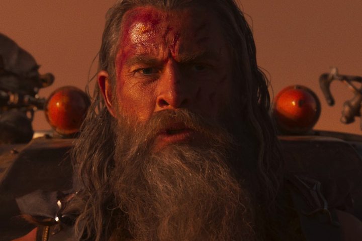 Chris Hemsworth sits on a truck hood in Furiosa: A Mad Max Saga.