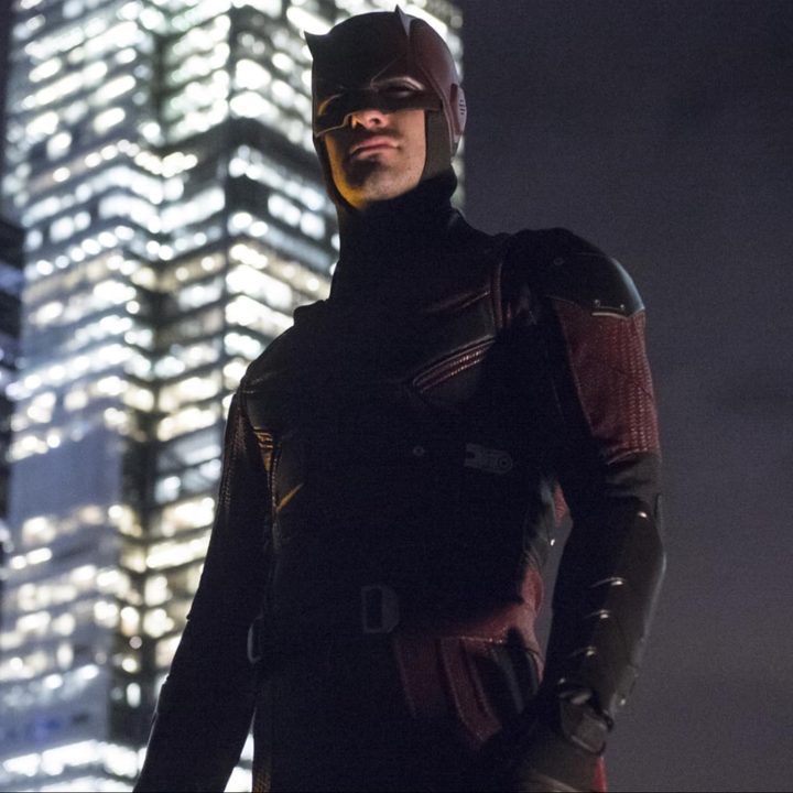 Daredevil stands on a roof with the city behind it.