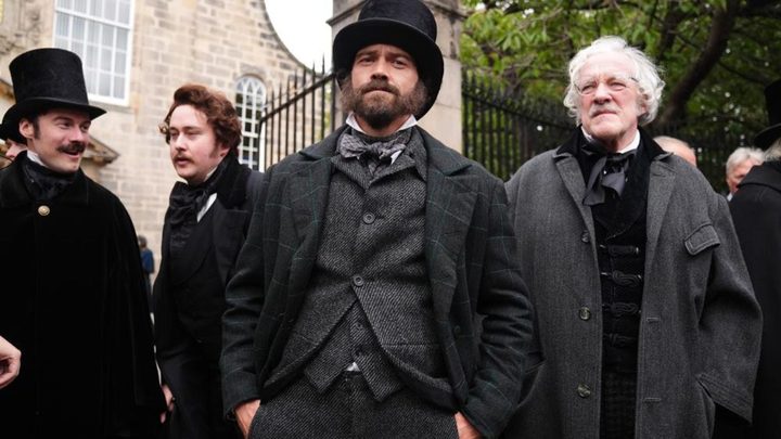 A group of Victorian men looking ahead while standing outside in Guillermo del Toro's Frankenstein.