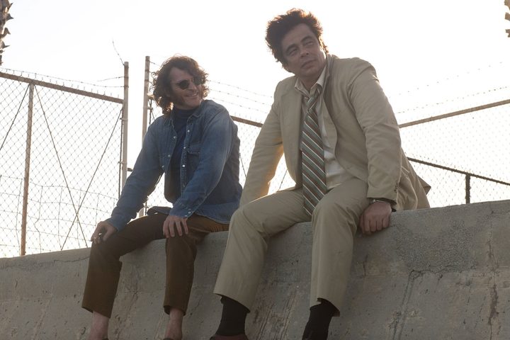 Joaquin Phoenix and Benicio Del Toro sit on a concrete divider in Inherent Vice.