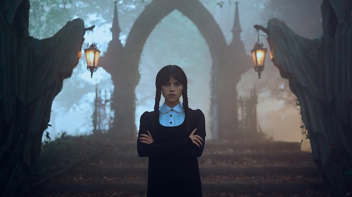 Jenna Ortega stands in front of steps with her hands crossed.
