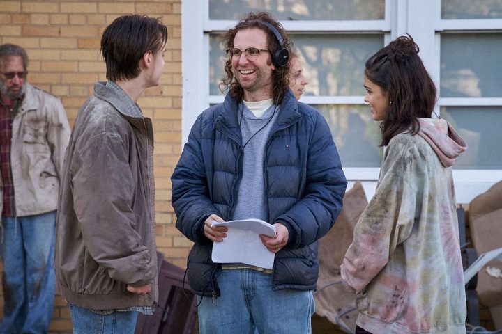 A man with headphones on stands between a boy and a girl in Y2K.