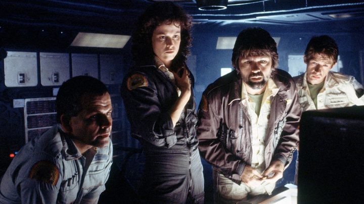 Four people gather around a computer while on a ship in Alien.