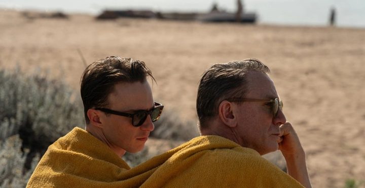 Two men sit on a beach in Queer.