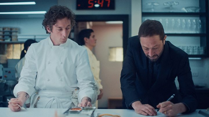 Carmy in his chef jacket looking at Richie writing something down in The Bear.