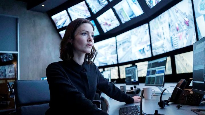 A woman sits in front of a wall of screens in The Capture.