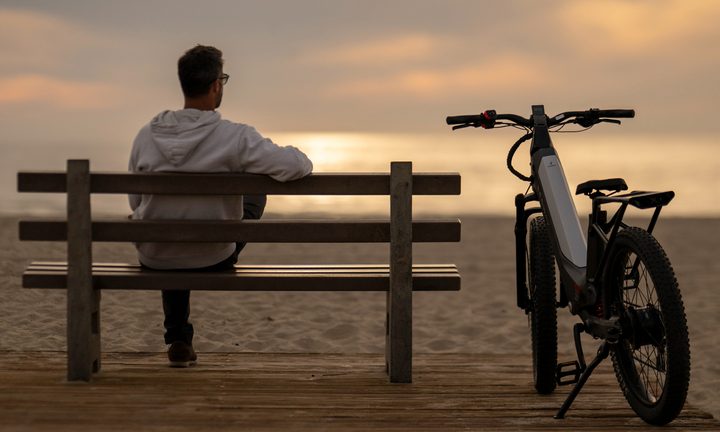Segway Xafari e-Bike parked by a bench at the beach with a person sitting on the bench.