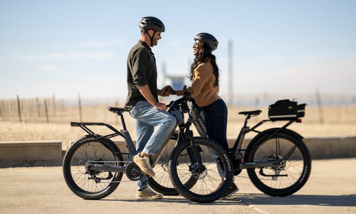 Two people with Segway Xafari e-bikes facing each other with blurry beach in the background.