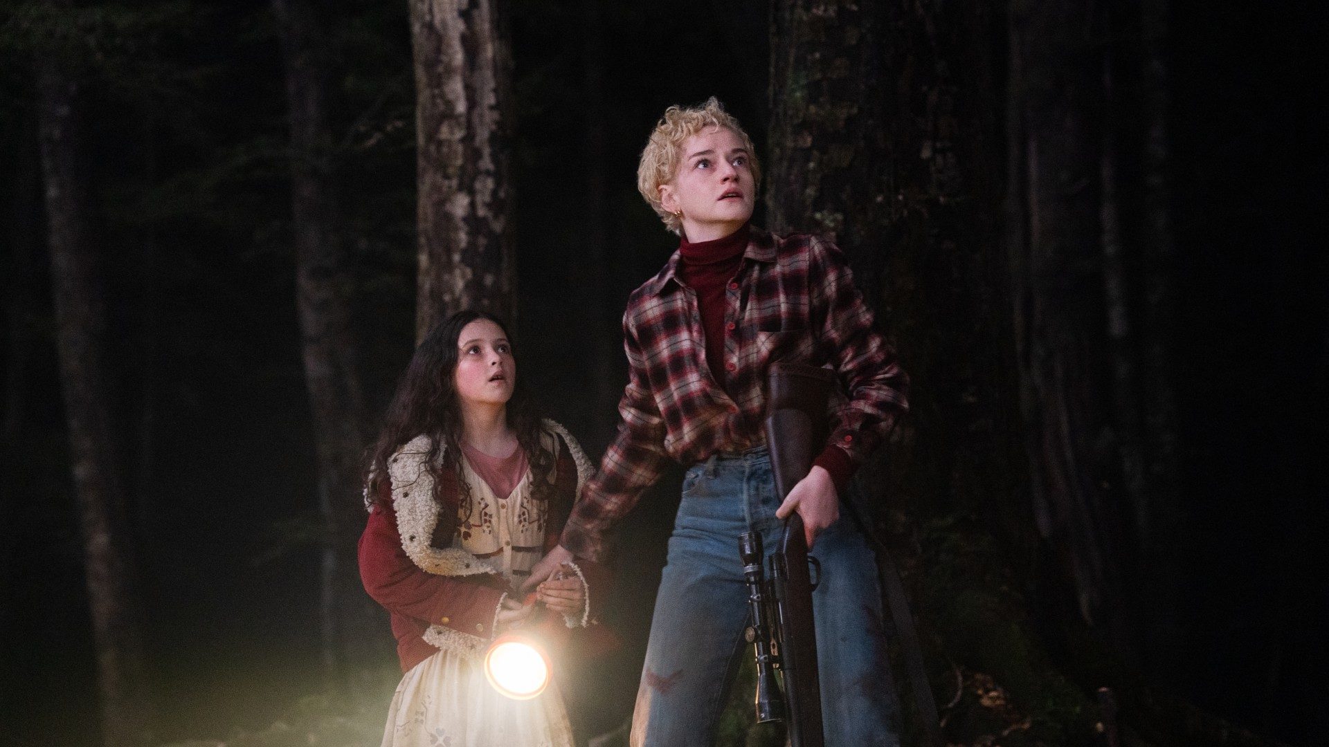 Matilda Firth and Julia Garner look scared in the woods in a still from the movie Wolf Man.