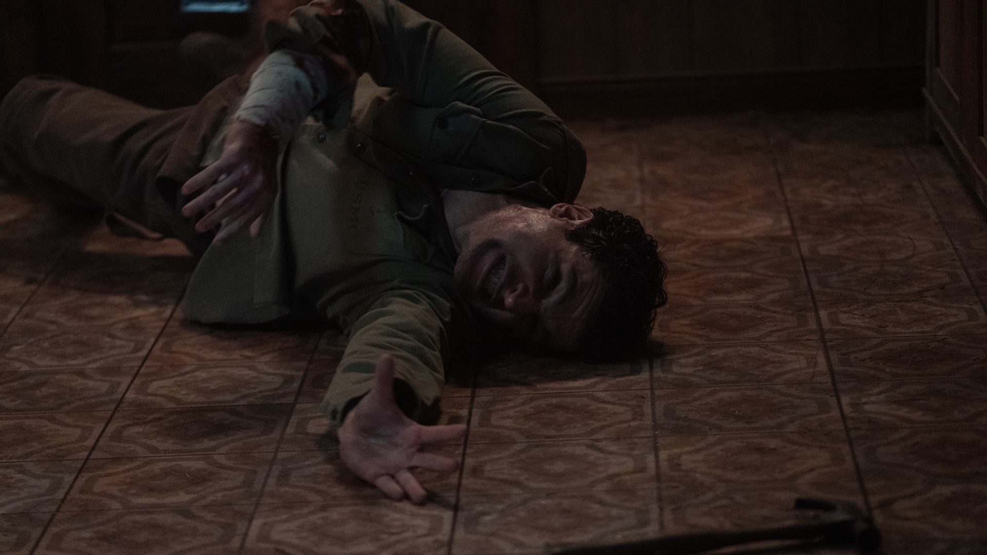 Christopher Abbott writhes on the floor and reaches for a hammer in a still from the movie Wolf Man.