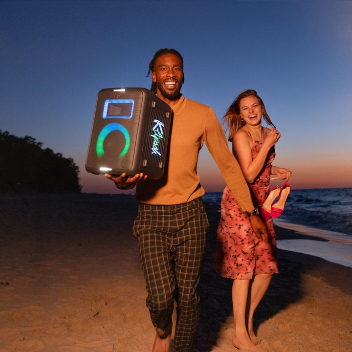 The Klipsch Vegas party speaker being held by a man walking on a beach with a woman.