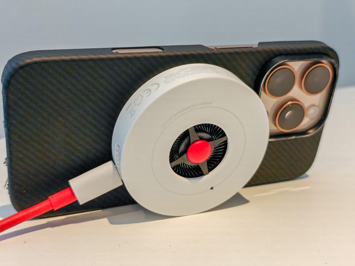 The OnePlus 50W AirVOOC charger attached to an iPhone 16 Pro propped up on a desk