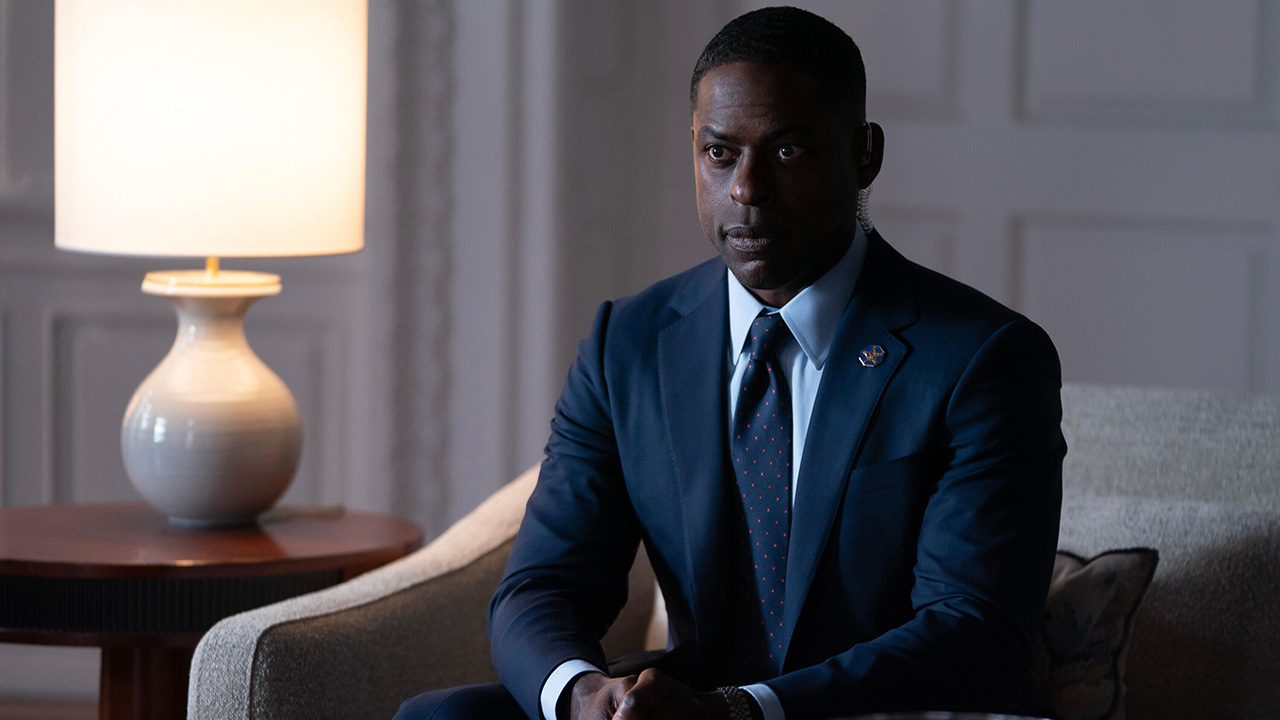 Xavier sitting upright in the Oval Office in a suit in Paradise.