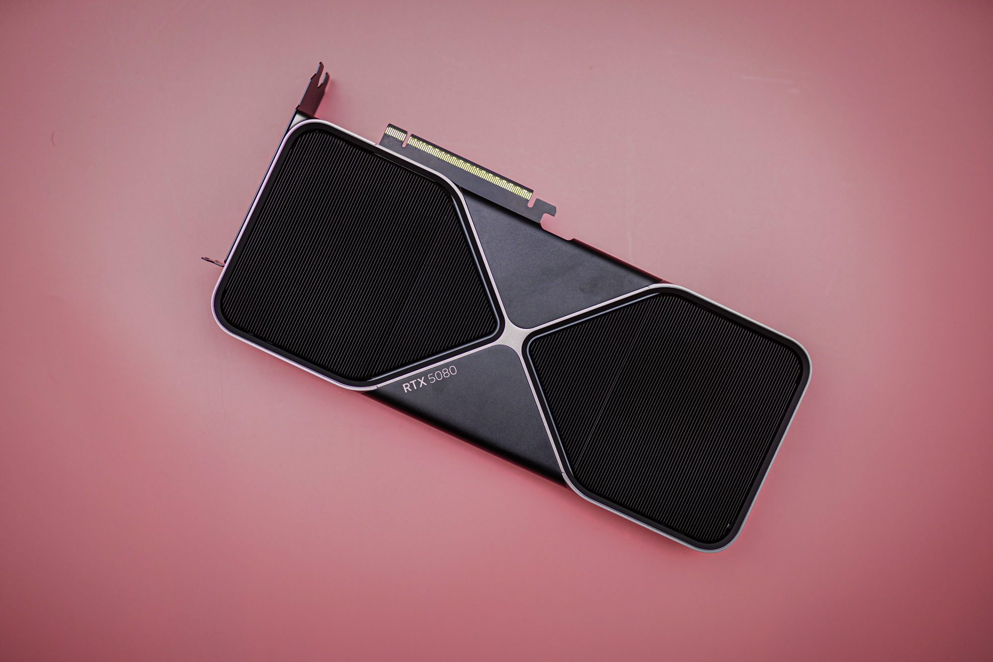The RTX 5080 sitting on a pink background.