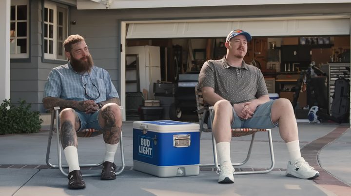 Post Malone and Shane Gillis sitting together in an ad for Bud Light.