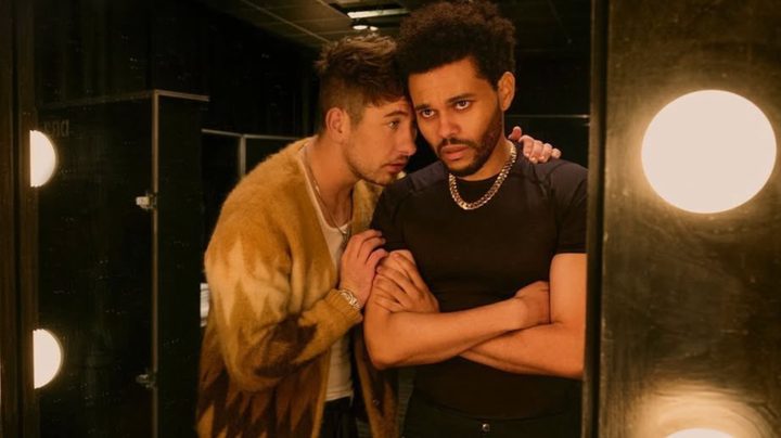 Barry Keoghan talks into The Weeknd's ear as they stare into a mirror.