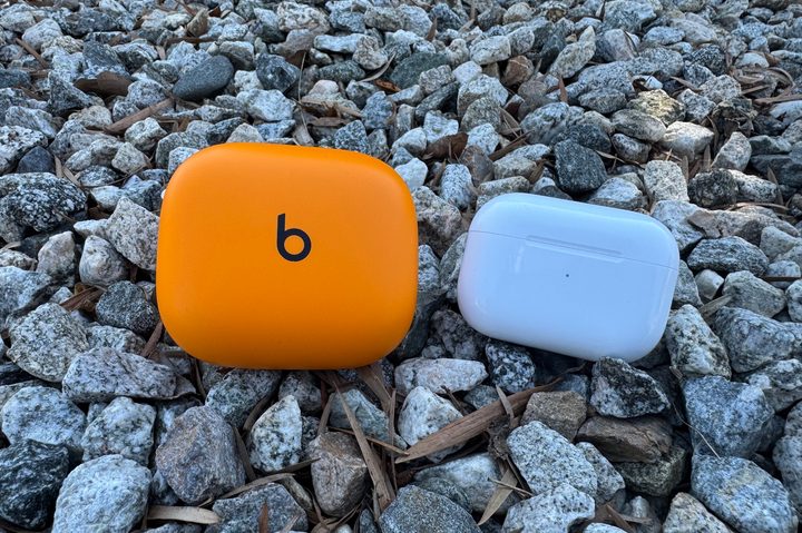 The Apple AirPods Pro 2 and Beats Powerbeats Pro 2 cases next to each other in some pebbles.
